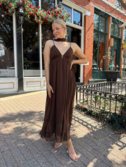 Woman wearing brown maxi dress with beaded detailing and detachable neck scarf.