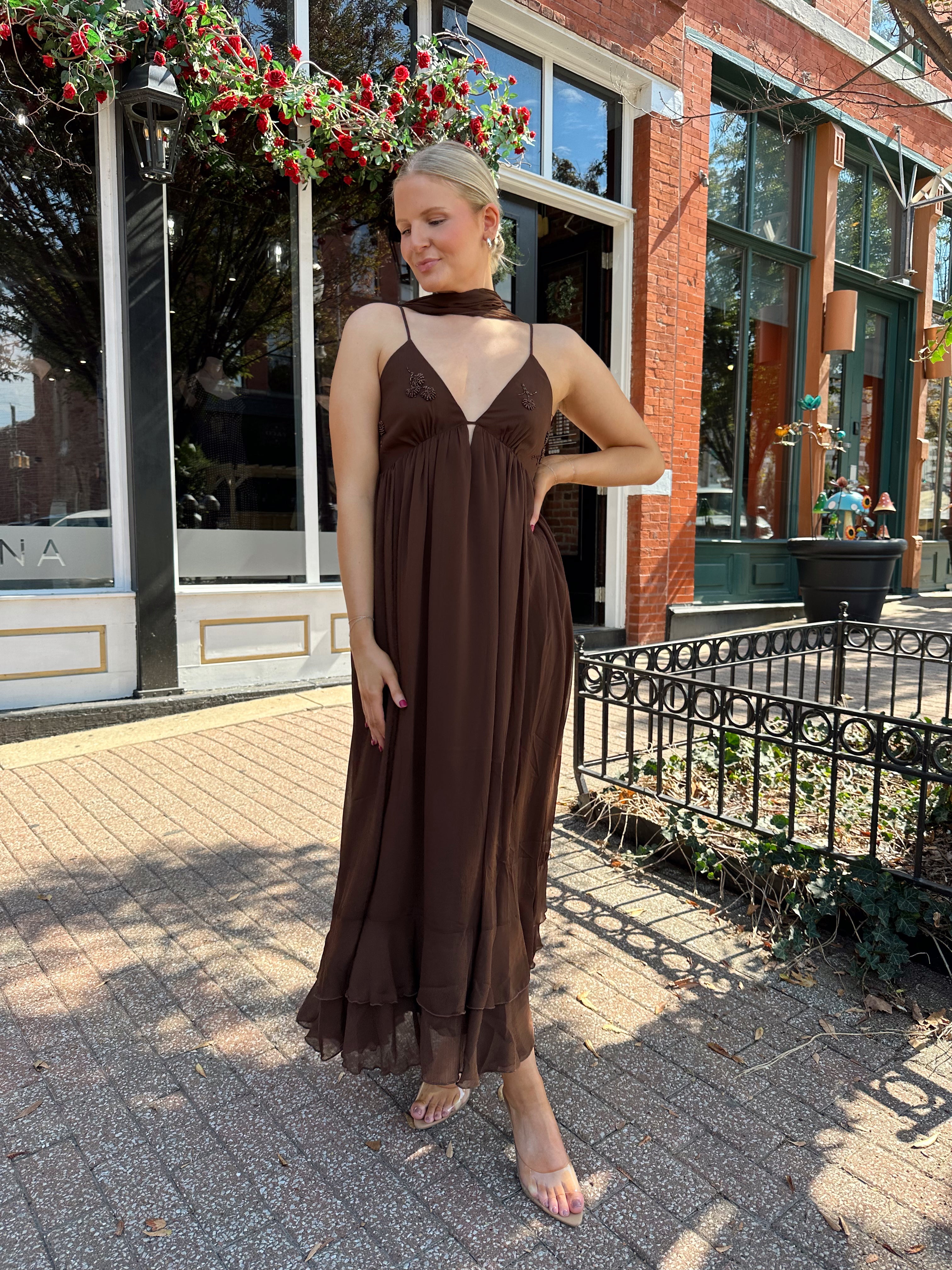Woman wearing brown maxi dress with beaded detailing and detachable neck scarf.