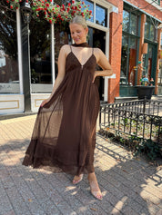 Woman wearing brown maxi dress with beaded detailing and detachable neck scarf.