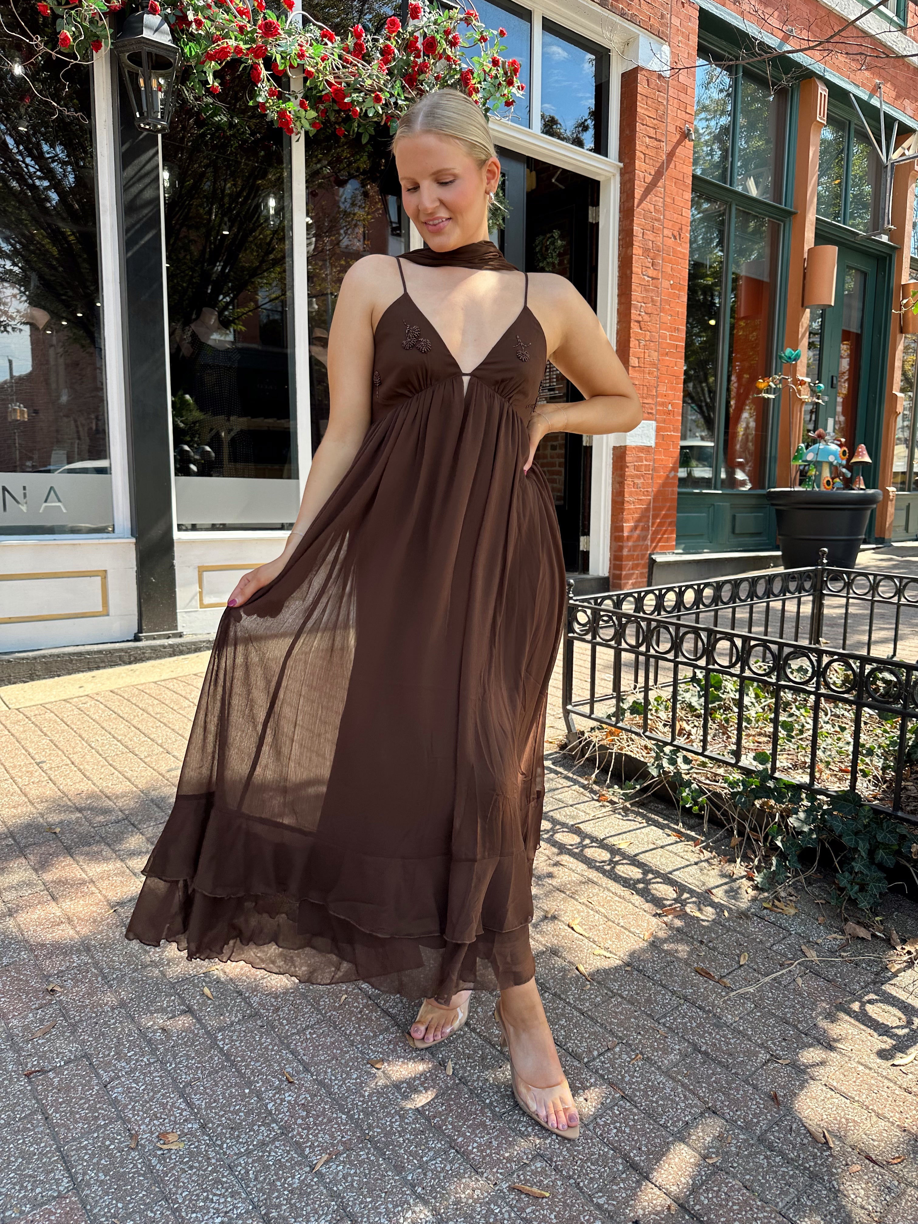 Woman wearing brown maxi dress with beaded detailing and detachable neck scarf.