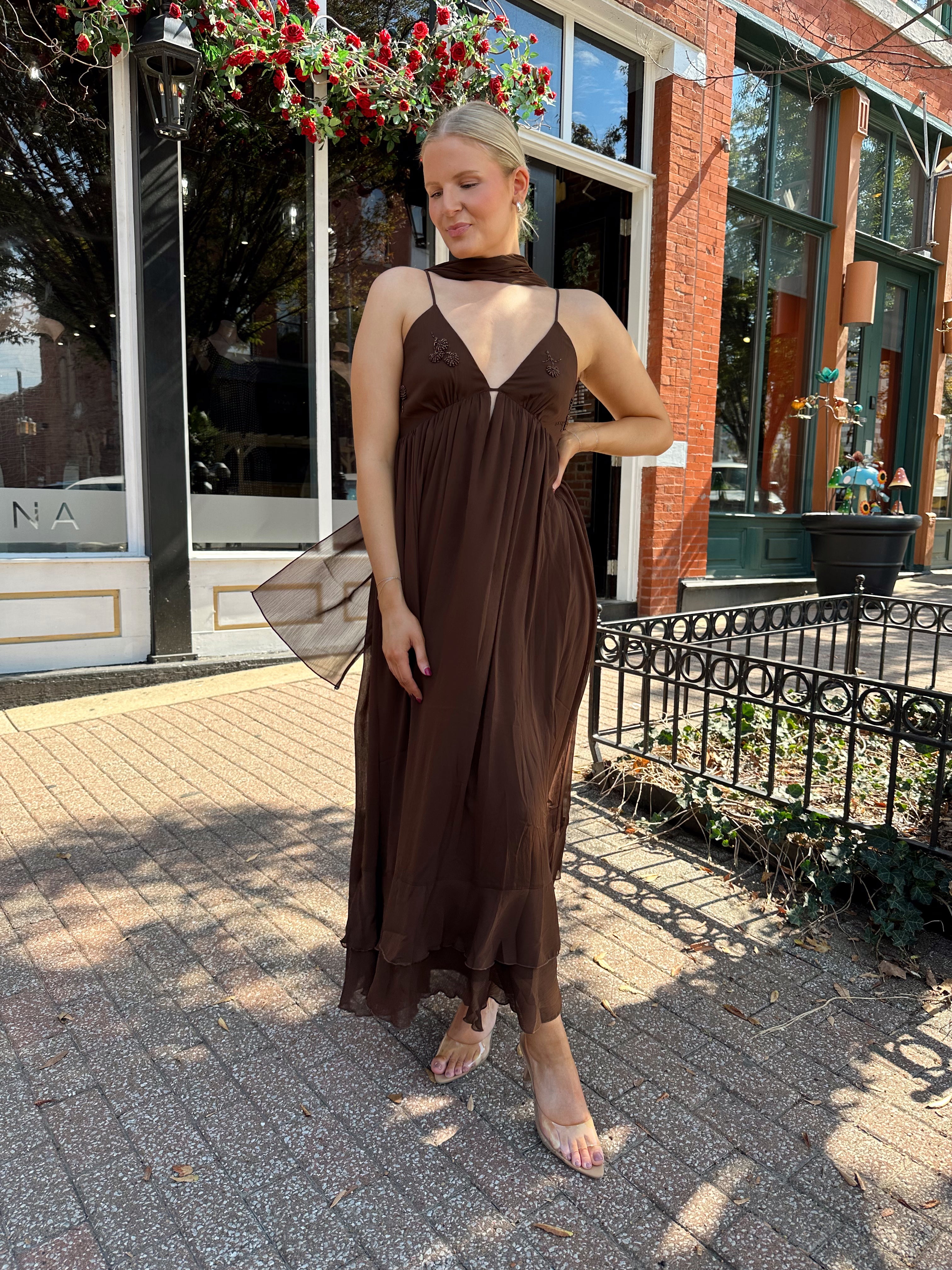 Woman wearing brown maxi dress with beaded detailing and detachable neck scarf.