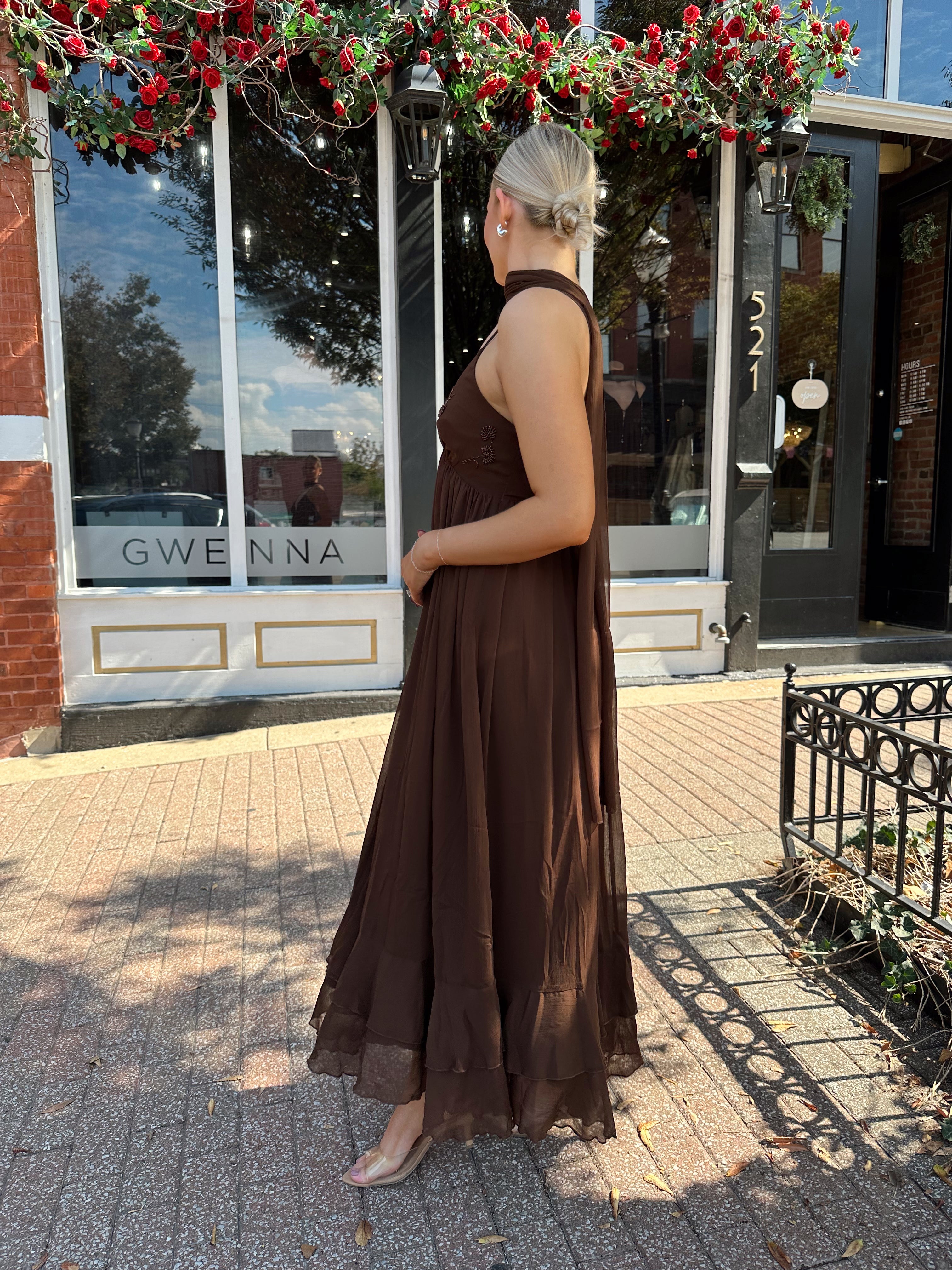 Woman wearing brown maxi dress with beaded detailing and detachable neck scarf.