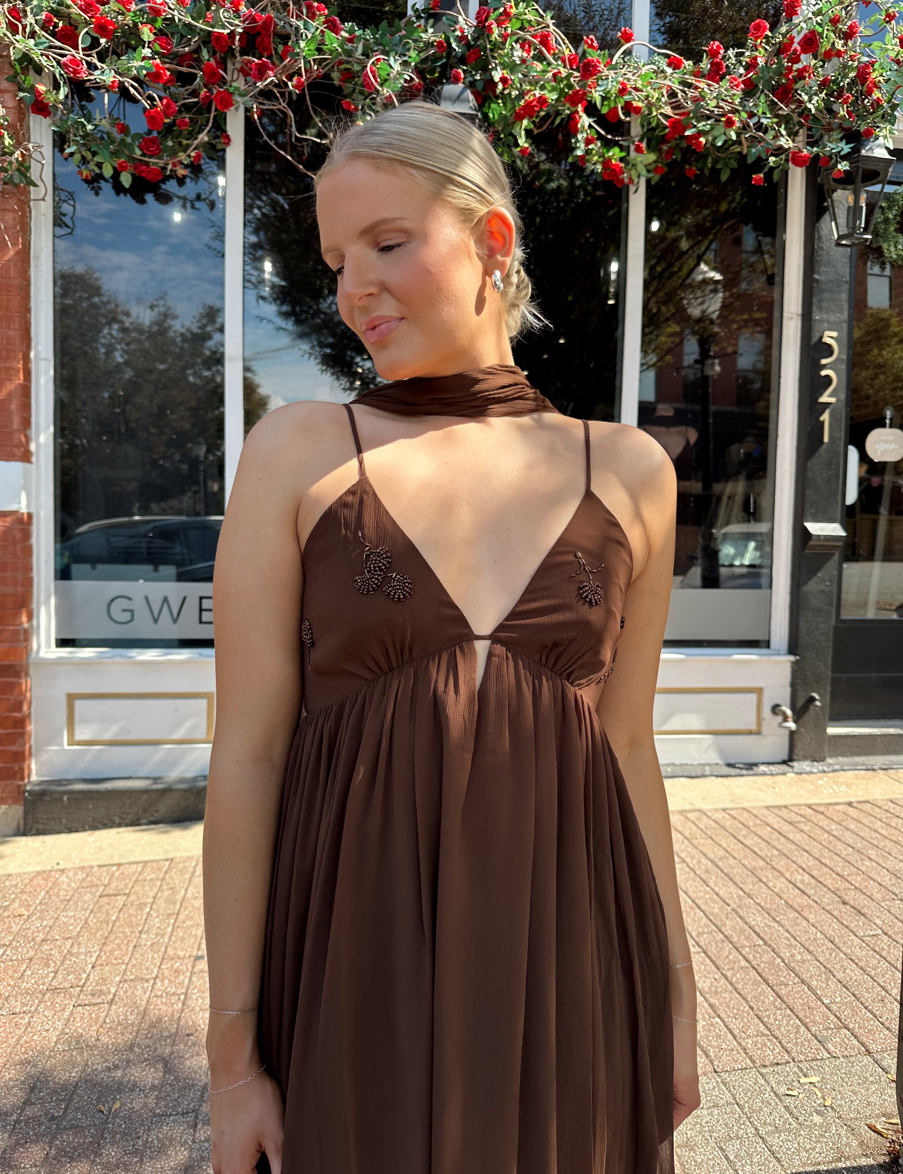Woman wearing brown maxi dress with beaded detailing and detachable neck scarf.
