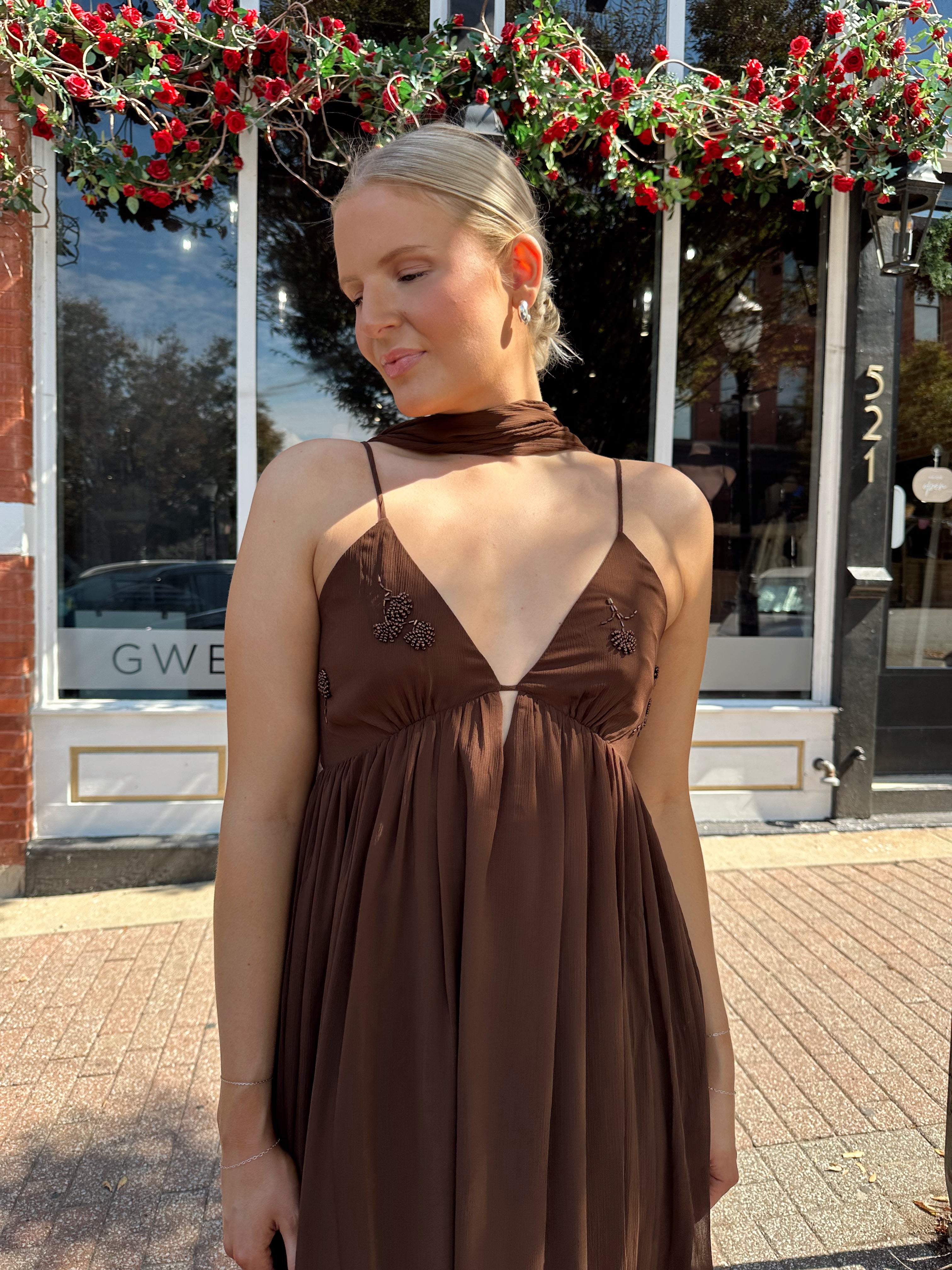 Woman wearing brown maxi dress with beaded detailing and detachable neck scarf.