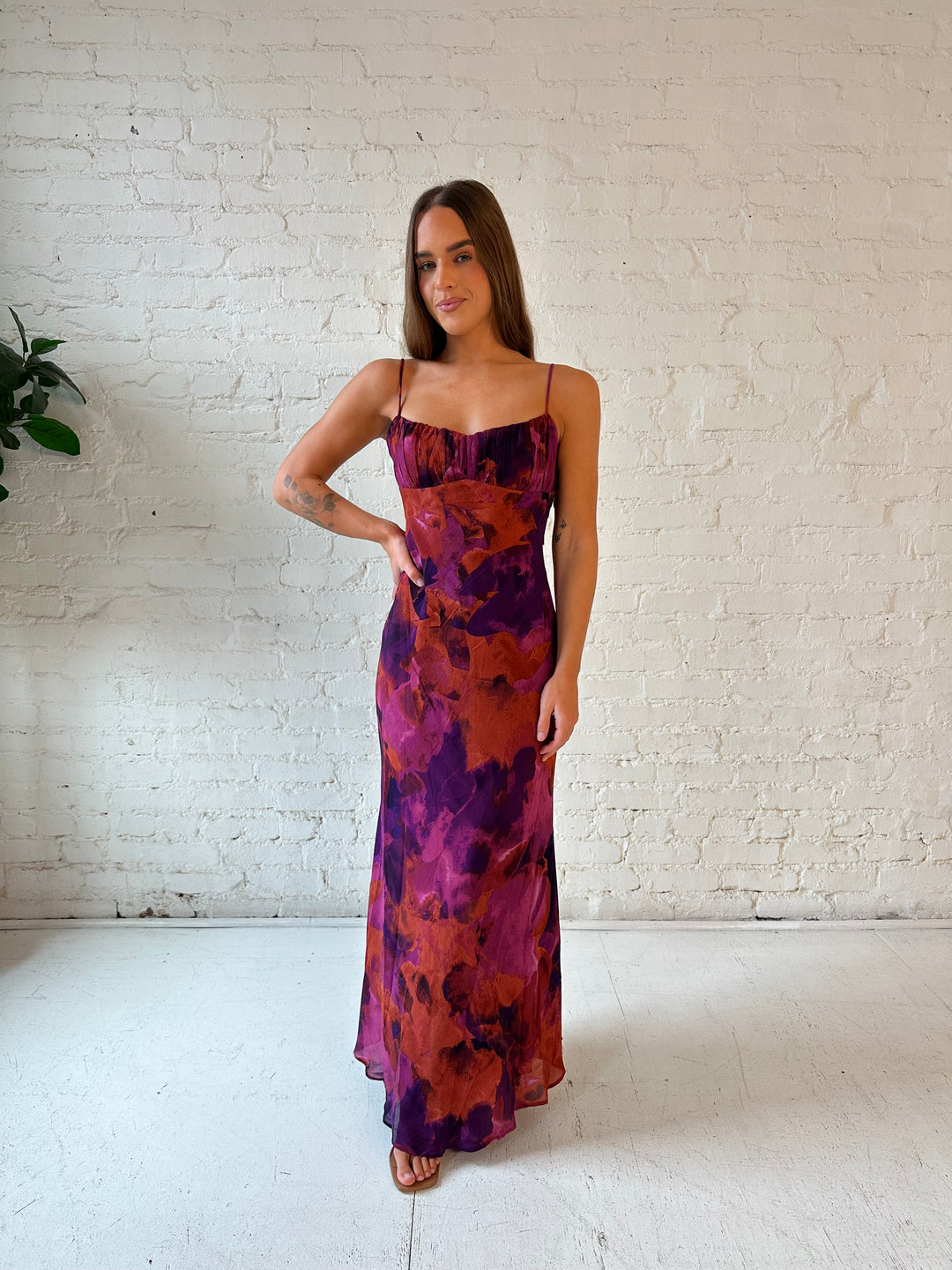Woman wearing dark floral maxi dress with open twist back, and adjustable spaghetti straps. 
