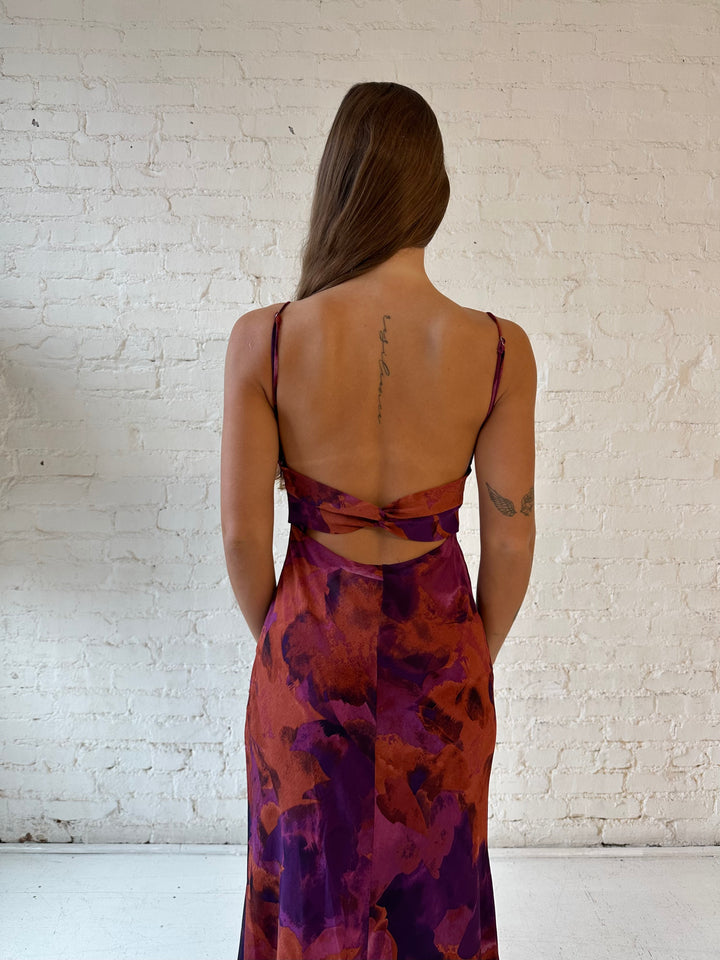 Woman wearing dark floral maxi dress with open twist back, and adjustable spaghetti straps. 
