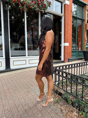 Woman wearing brown sequin shift mini dress with straight neckline and adjustable straps. 