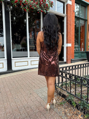 Woman wearing brown sequin shift mini dress with straight neckline and adjustable straps. 