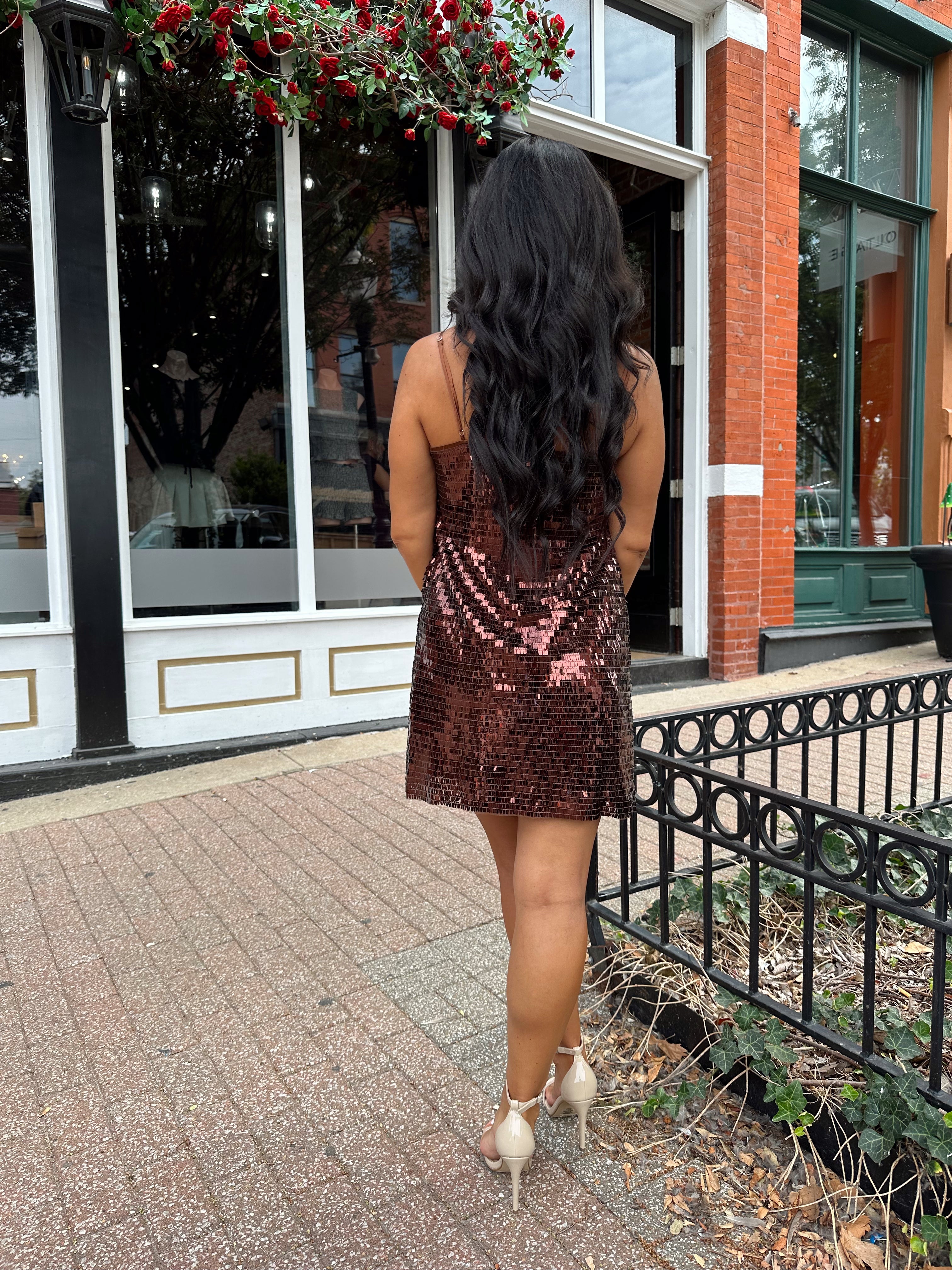 Woman wearing brown sequin shift mini dress with straight neckline and adjustable straps. 