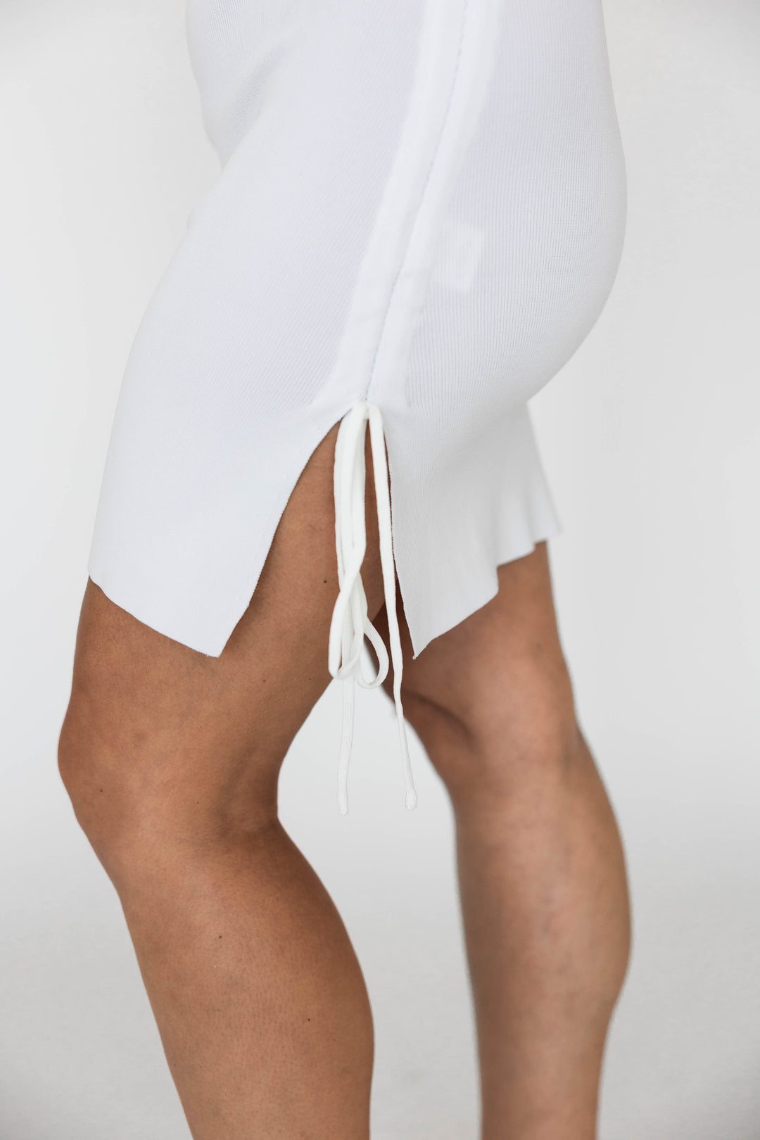 Woman wearing white mini dress with ruched side tie detailing. 