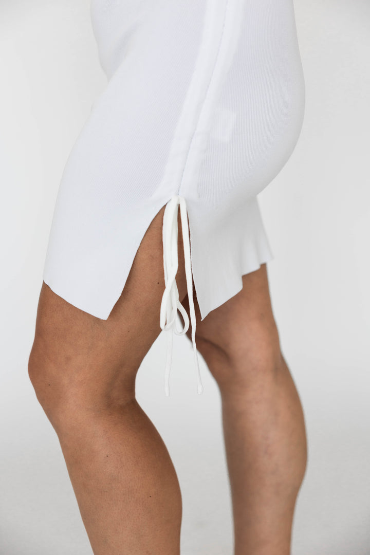 Woman wearing white mini dress with ruched side tie detailing. 