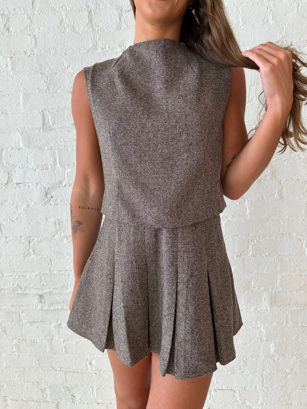 Woman wearing brown textured pleated mini skirt set with sleeveless mock neck top.