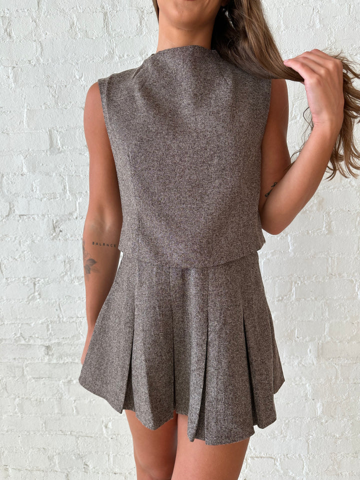 Woman wearing brown textured pleated mini skirt set with sleeveless mock neck top.