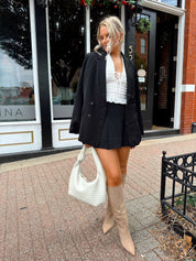 Woman wearing black tailored oversize blazer with collar and button closure. 