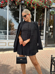 Woman wearing tailored oversized blazer over top of black polka dot mini dress.