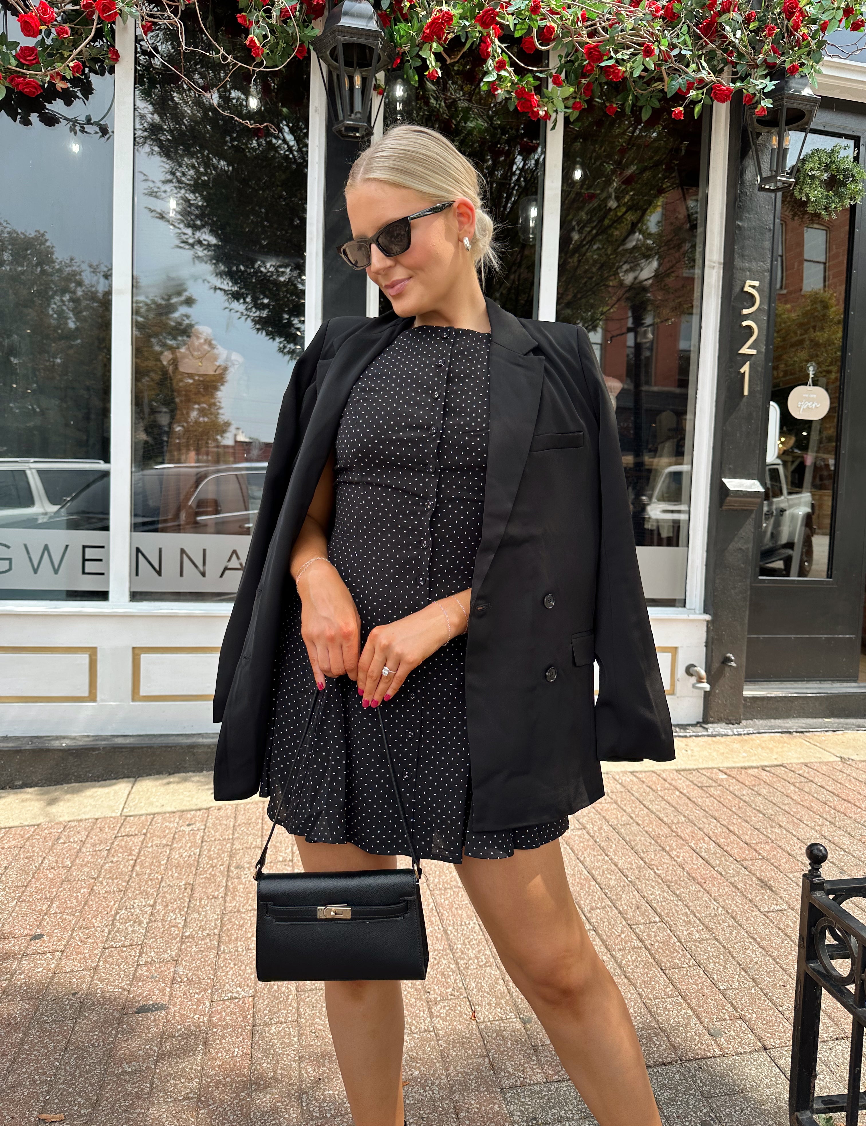 Woman wearing tailored oversized blazer over top of black polka dot mini dress.