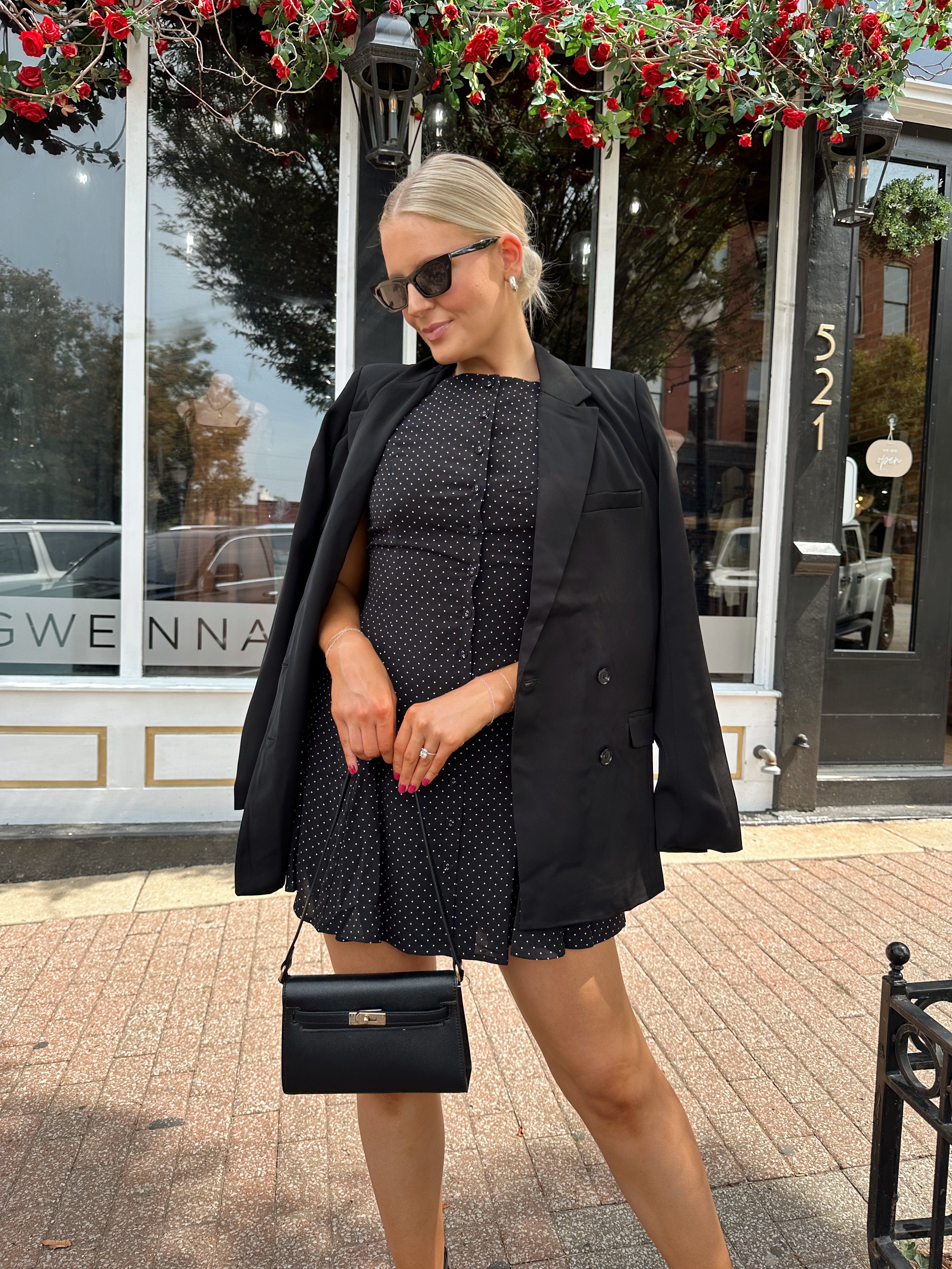 Woman wearing tailored oversized blazer over top of black polka dot mini dress.