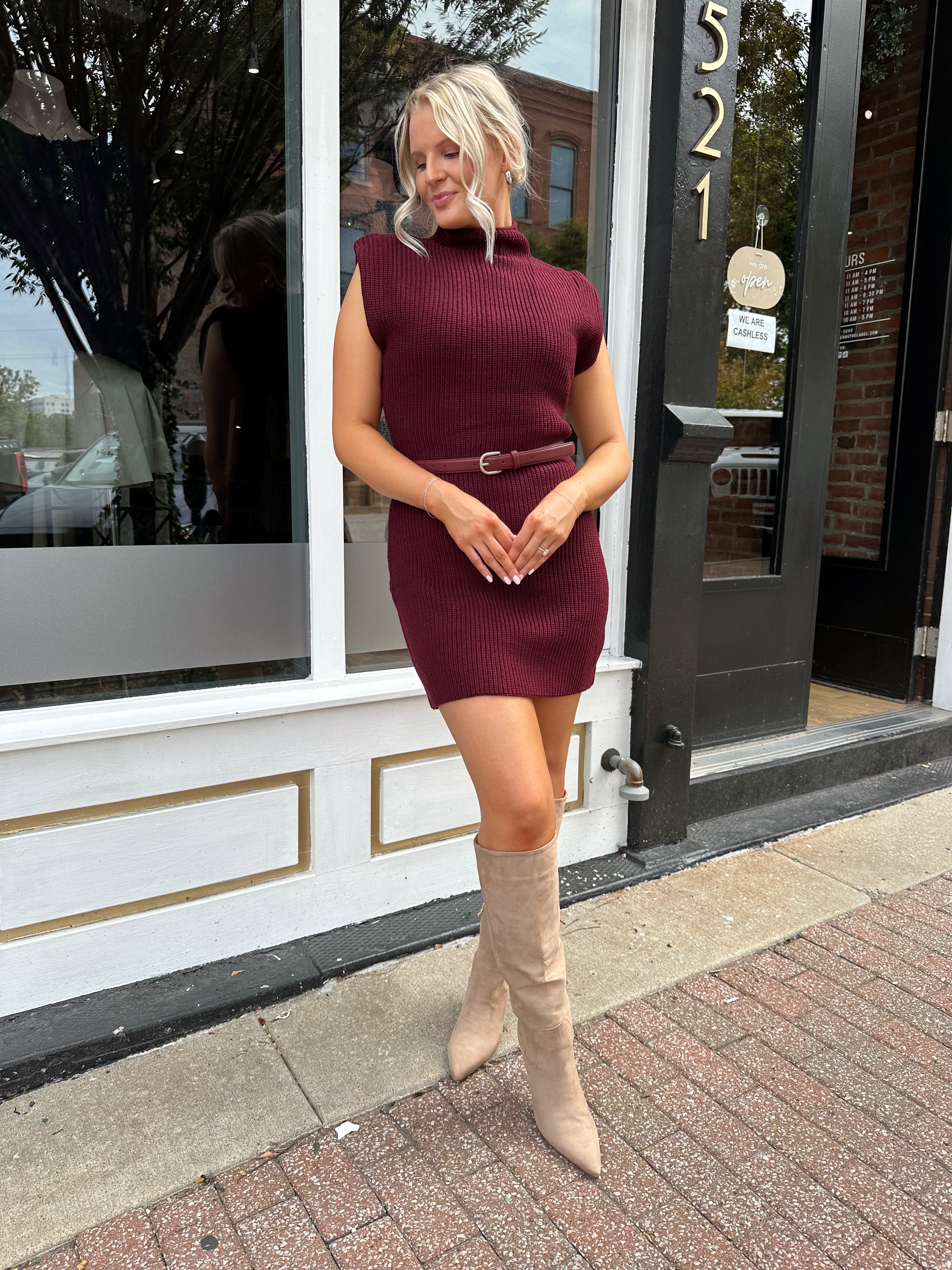 Woman wearing burgundy ribbed sweater mini dress with belted waist and mock neck.