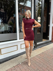 Woman wearing burgundy ribbed sweater mini dress with belted waist and mock neck.