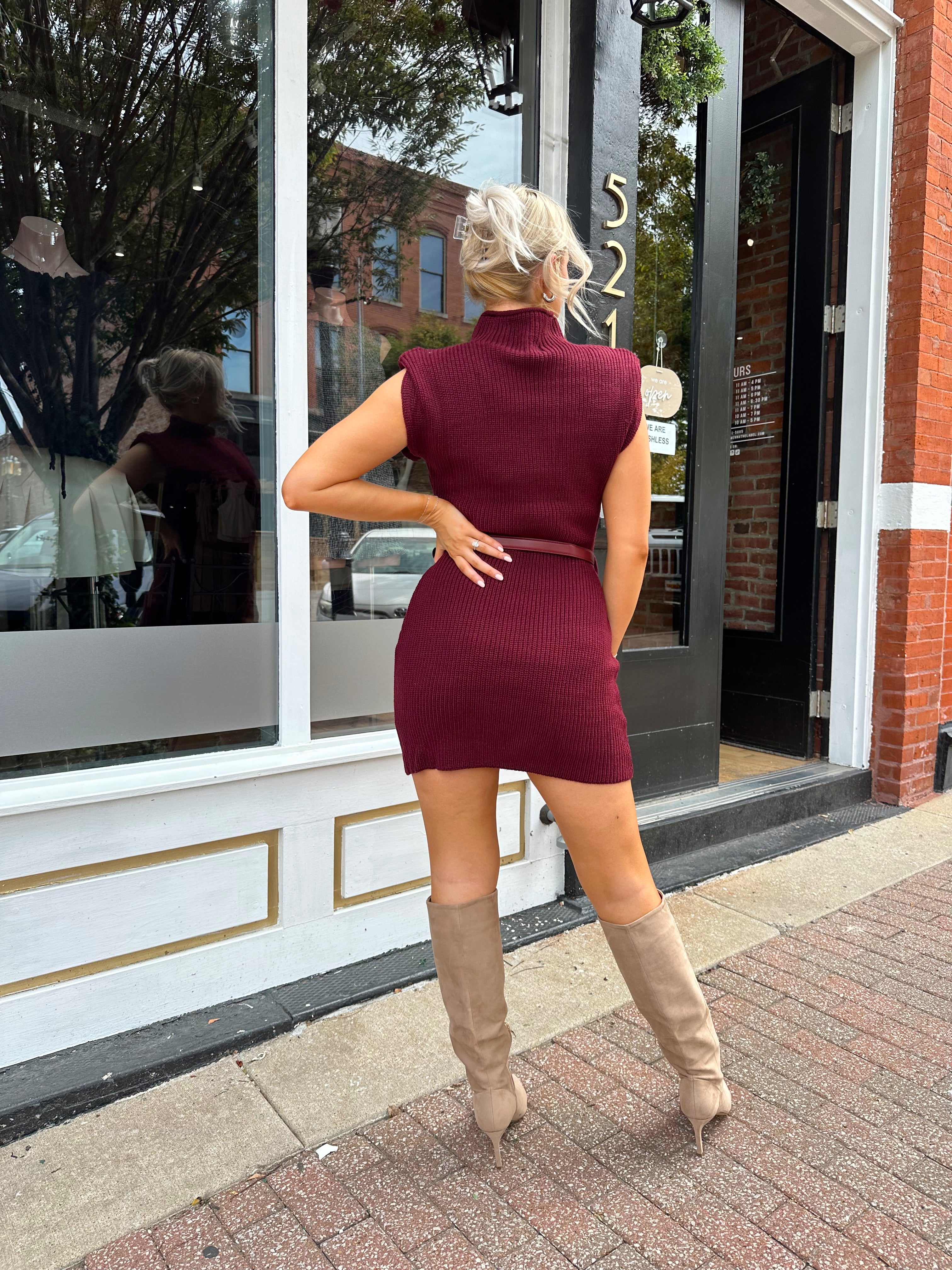 Woman wearing burgundy ribbed sweater mini dress with belted waist and mock neck.