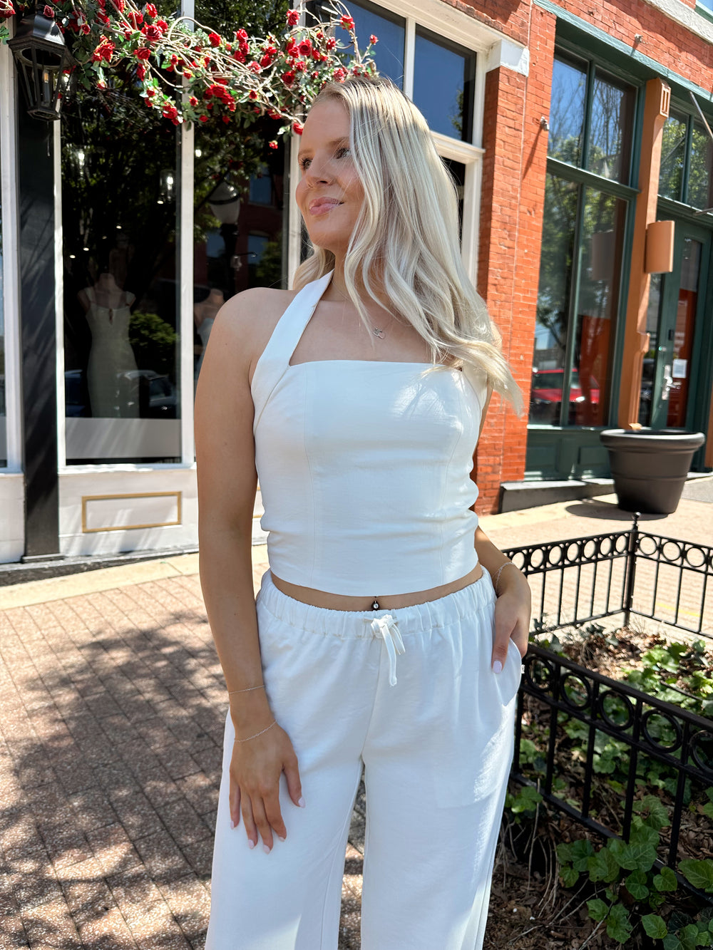 Woman wearing cream two piece pant set with square neck halter top. 