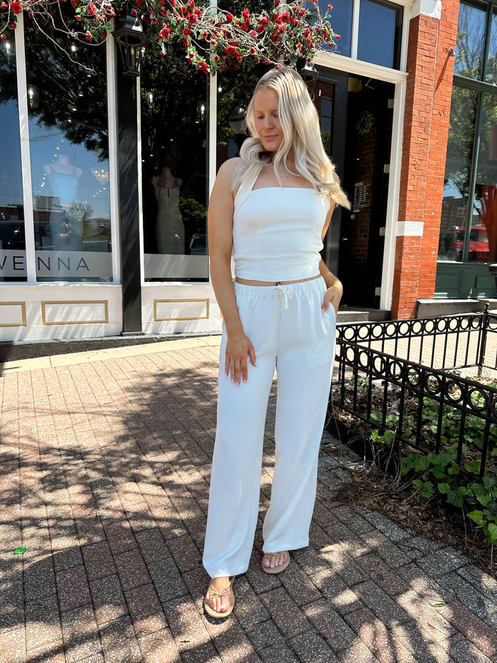 Woman wearing cream two piece pant set with square neck halter top. 