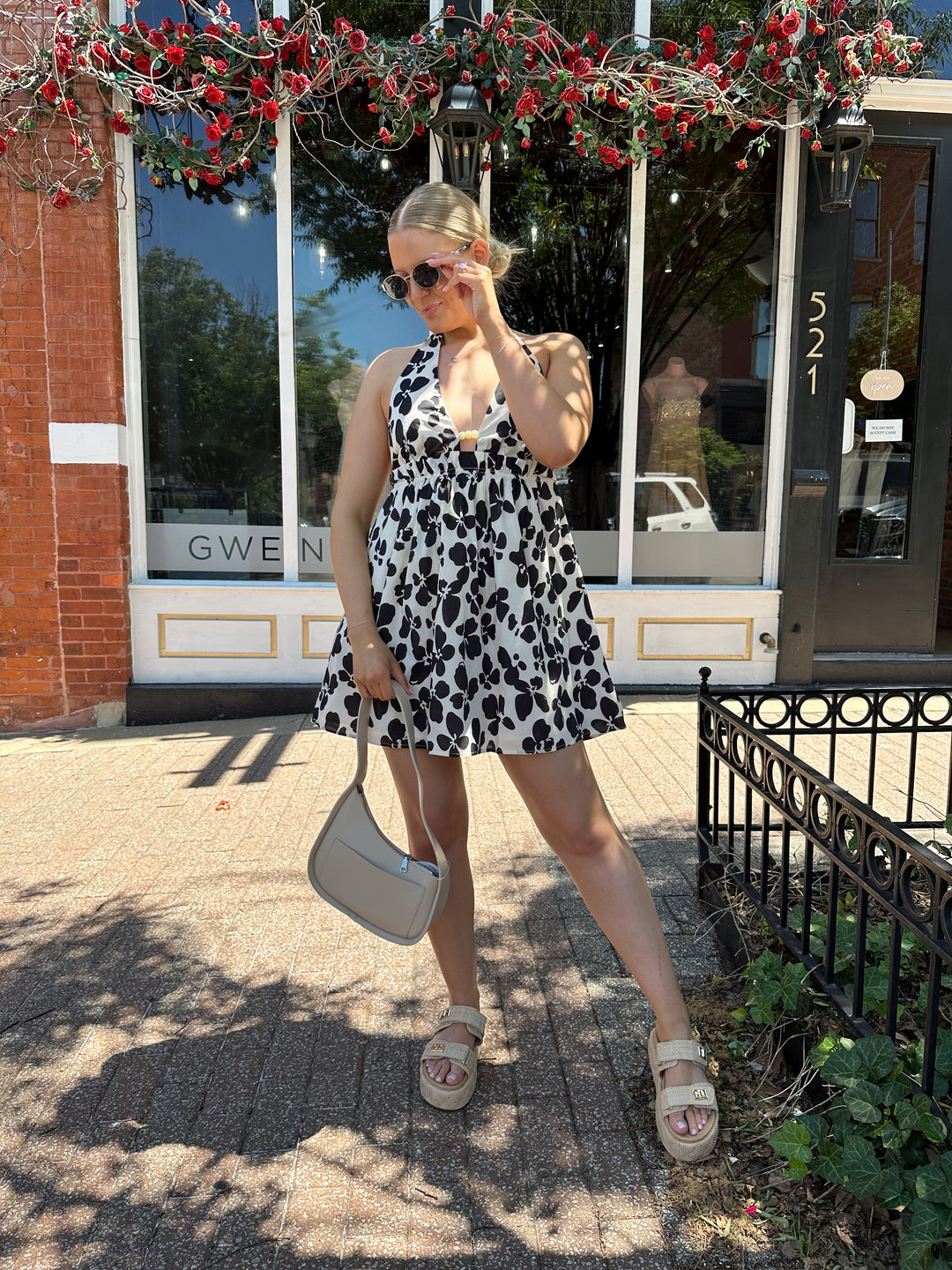 Woman wearing ivory and black floral mini dress with self tie halter neck, beading, and elastic cinched waist. 