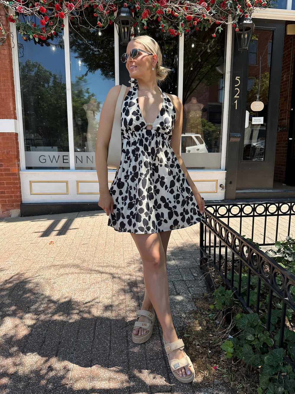 Woman wearing ivory and black floral mini dress with self tie halter neck, beading, and elastic cinched waist. 
