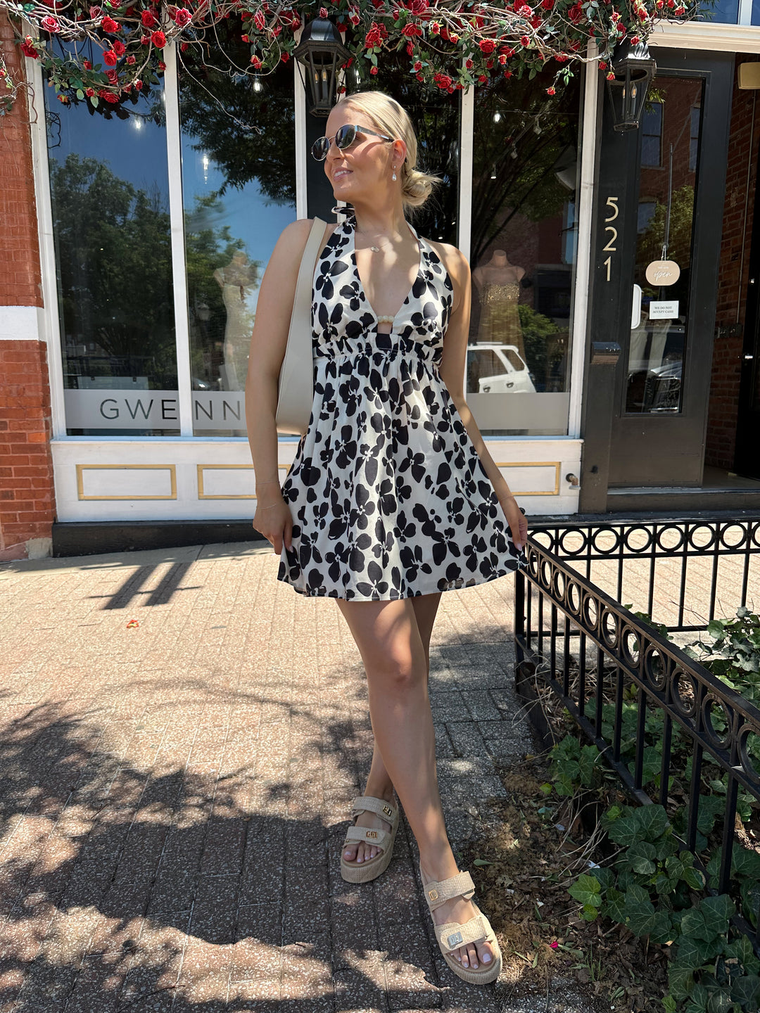 Woman wearing ivory and black floral mini dress with self tie halter neck, beading, and elastic cinched waist. 