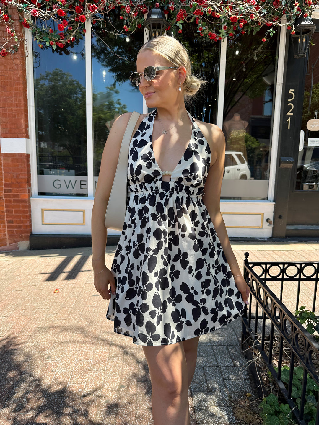 Woman wearing ivory and black floral mini dress with self tie halter neck, beading, and elastic cinched waist. 