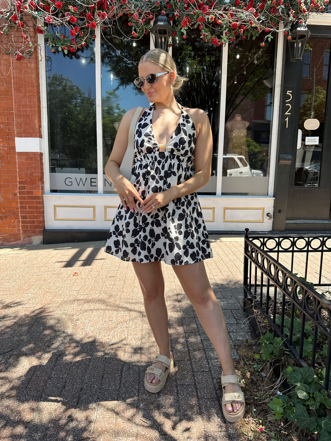 Woman wearing ivory and black floral mini dress with self tie halter neck, beading, and elastic cinched waist. 