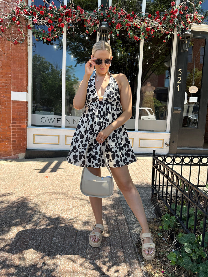 Woman wearing ivory and black floral mini dress with self tie halter neck, beading, and elastic cinched waist. 