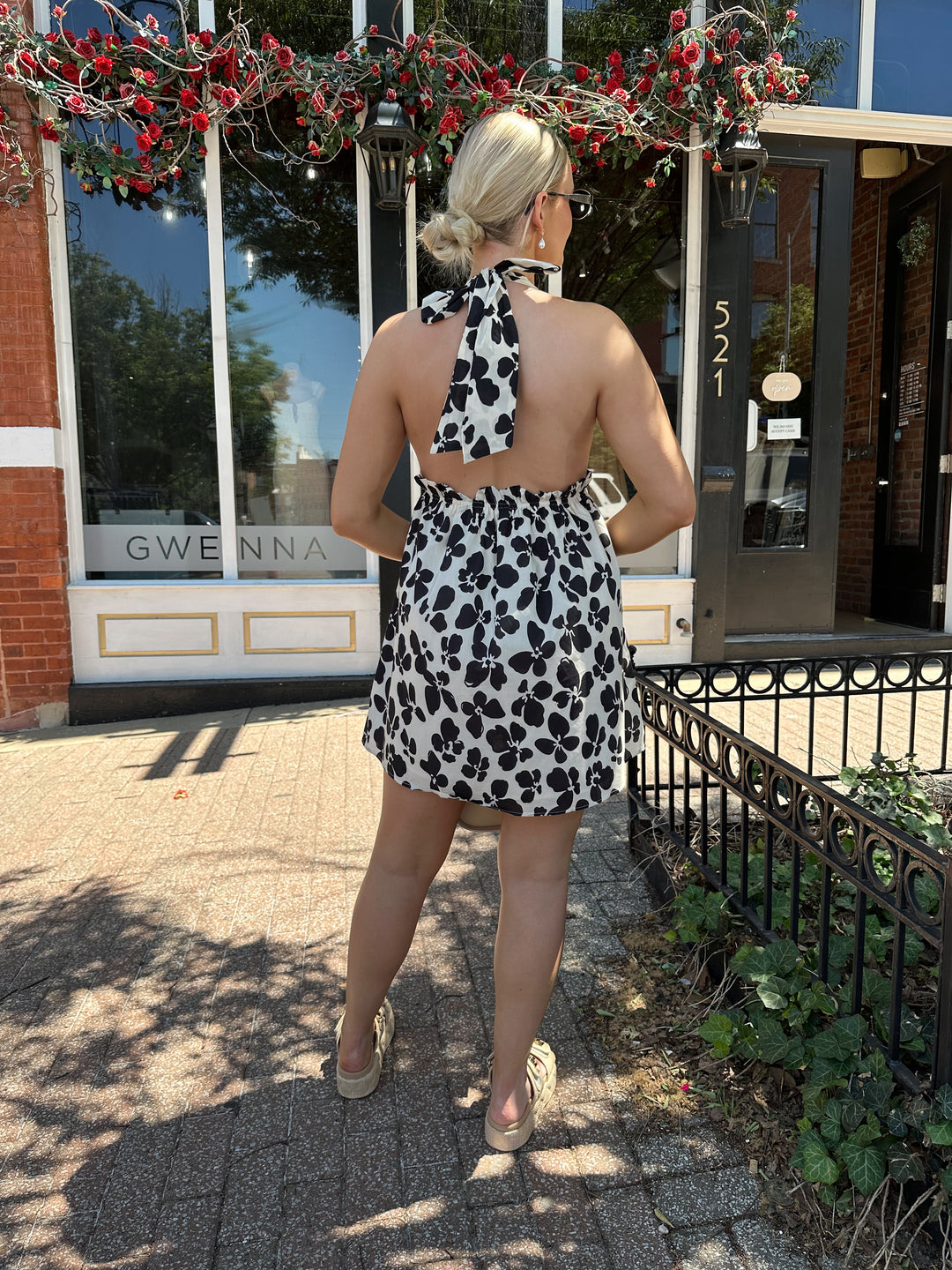 Woman wearing ivory and black floral mini dress with self tie halter neck, beading, and elastic cinched waist. 