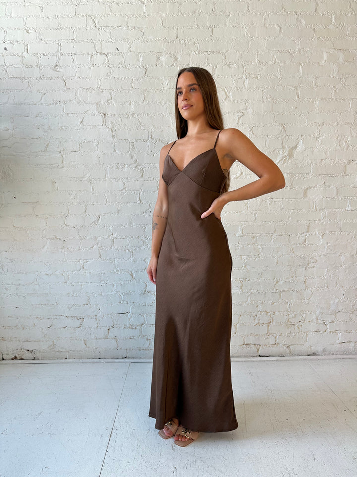 Woman wearing brown textured maxi dress with v-neckline and adjustable spaghetti straps. 