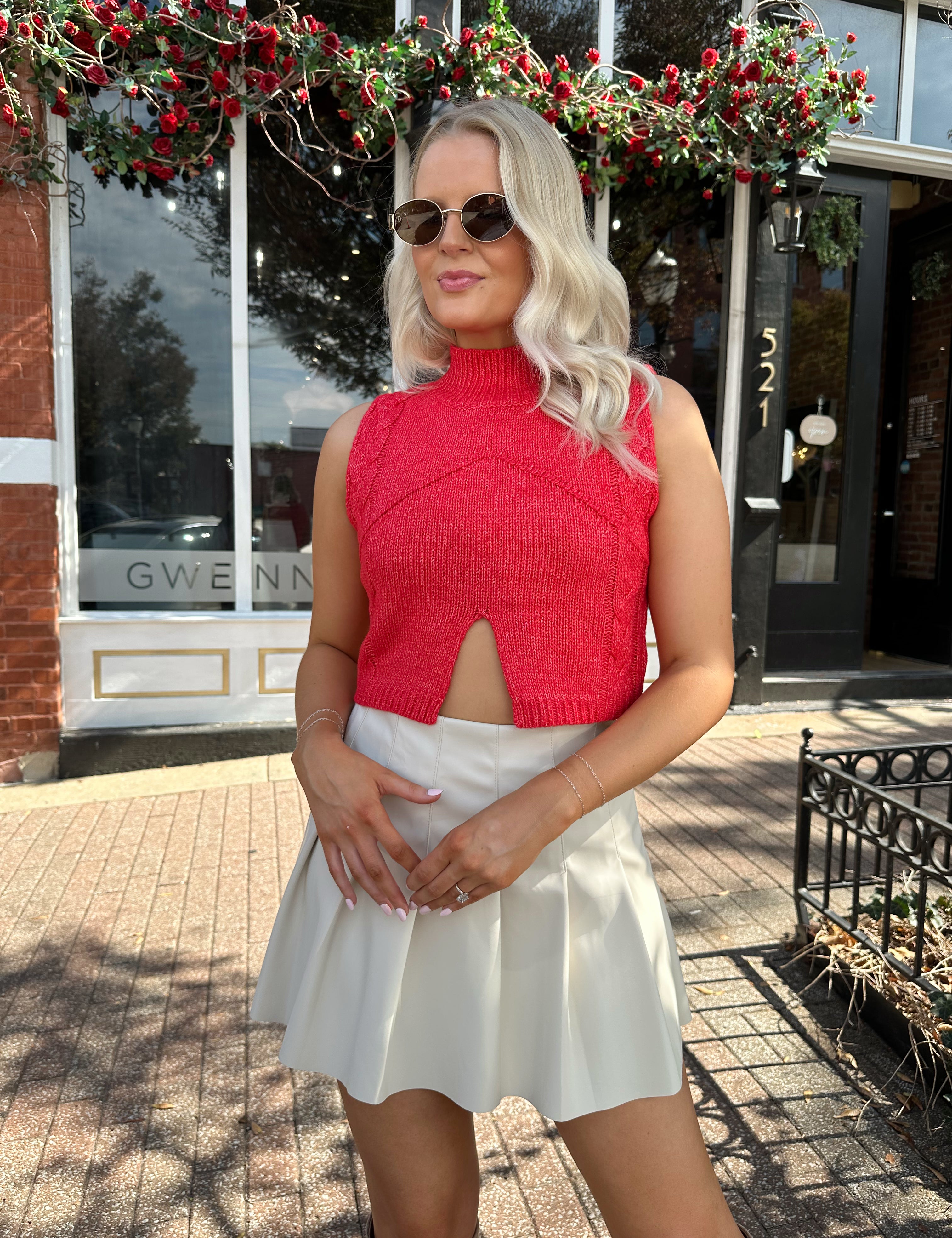 Woman wearing red sleeveless sweater tip with cream pleated leather mini skirt. 