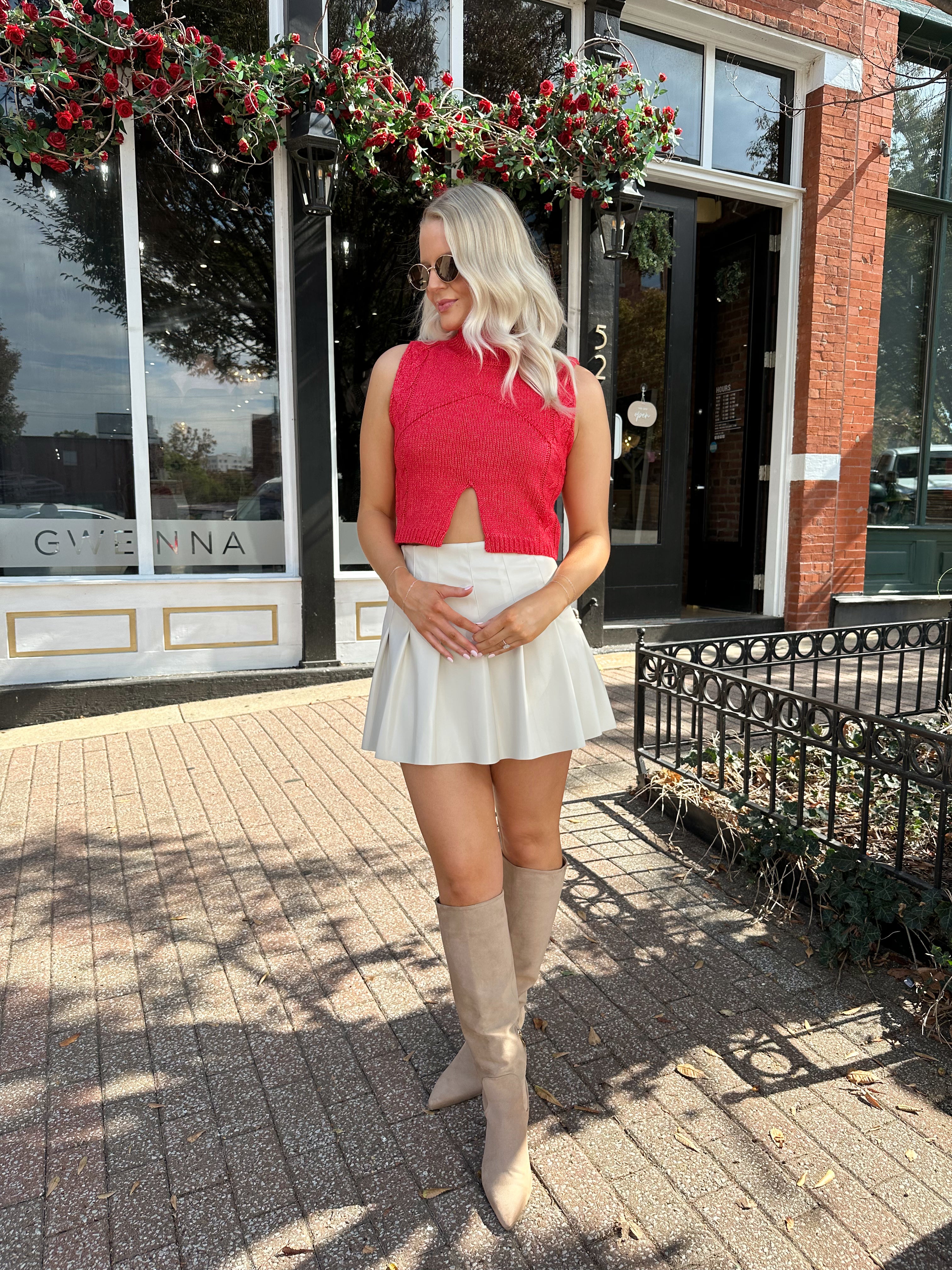 Woman wearing red sleeveless sweater tip with cream pleated leather mini skirt. 