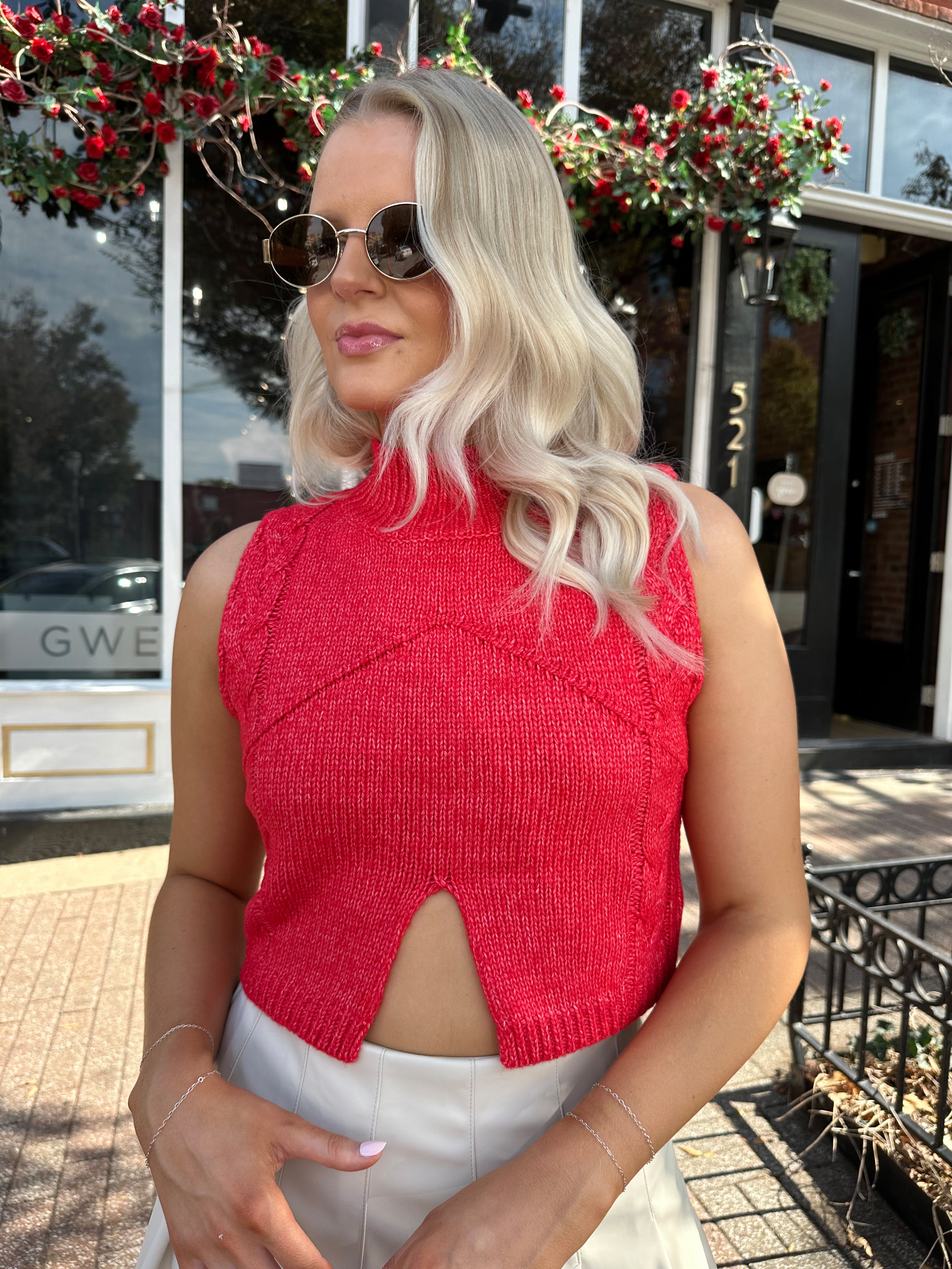Woman wearing red sleeveless sweater tip with cream pleated leather mini skirt. 