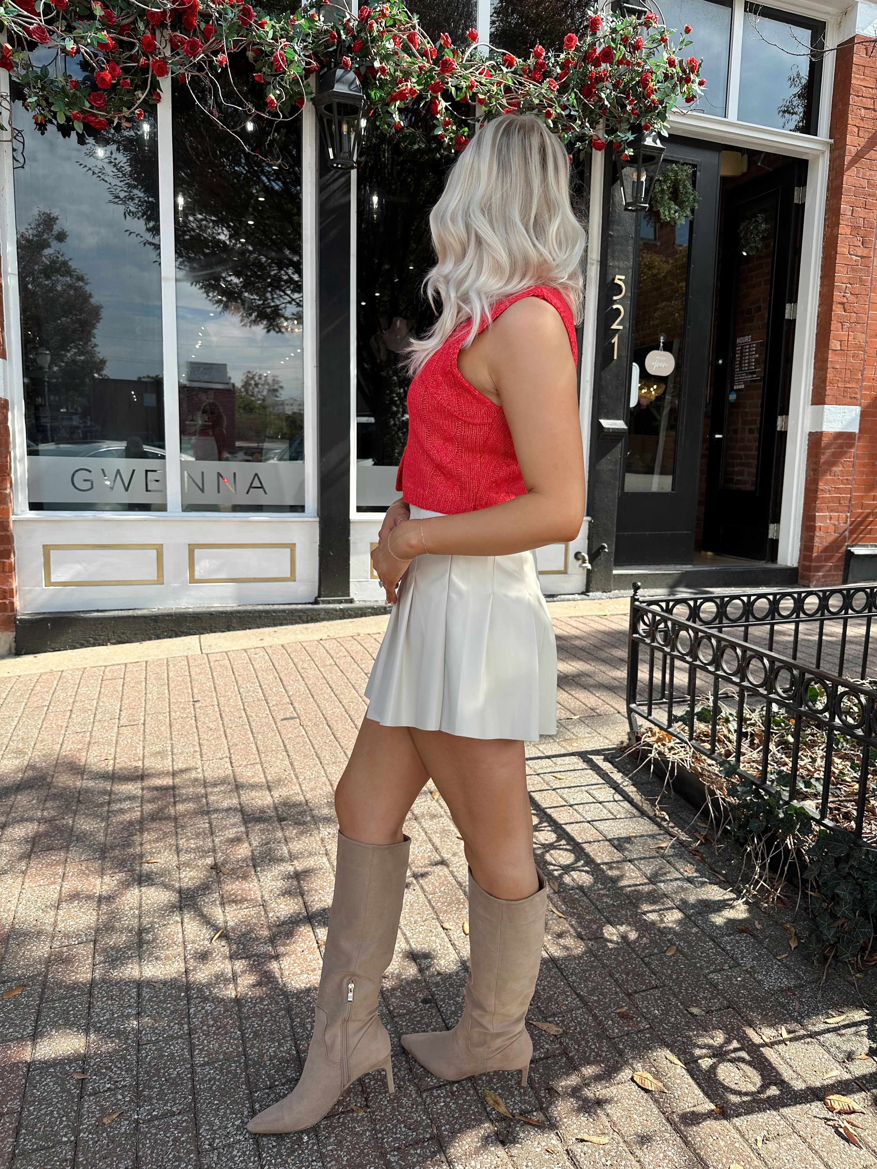 Woman wearing red sleeveless sweater tip with cream pleated leather mini skirt. 