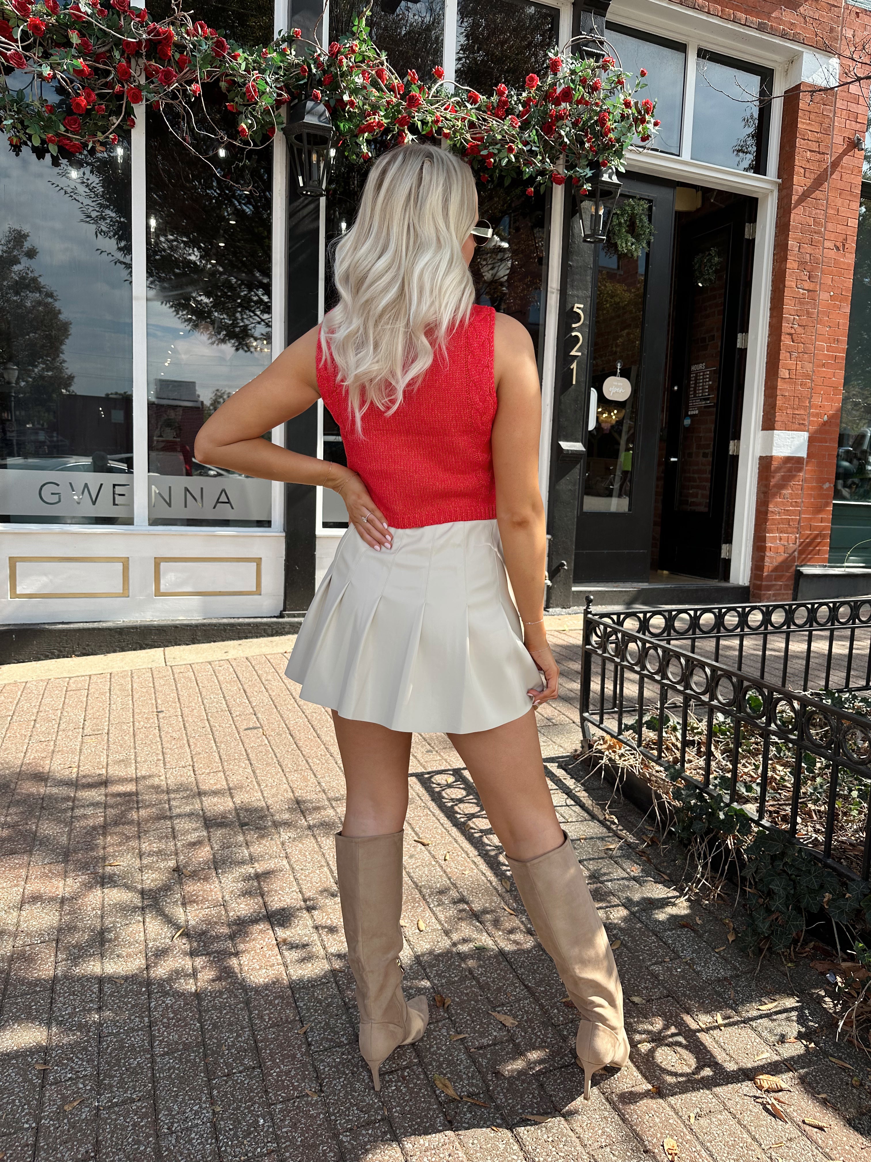 Woman wearing red sleeveless sweater tip with cream pleated leather mini skirt. 