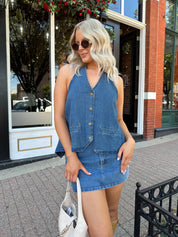 Woman wearing medium wash denim halter top with button closure and open back. 