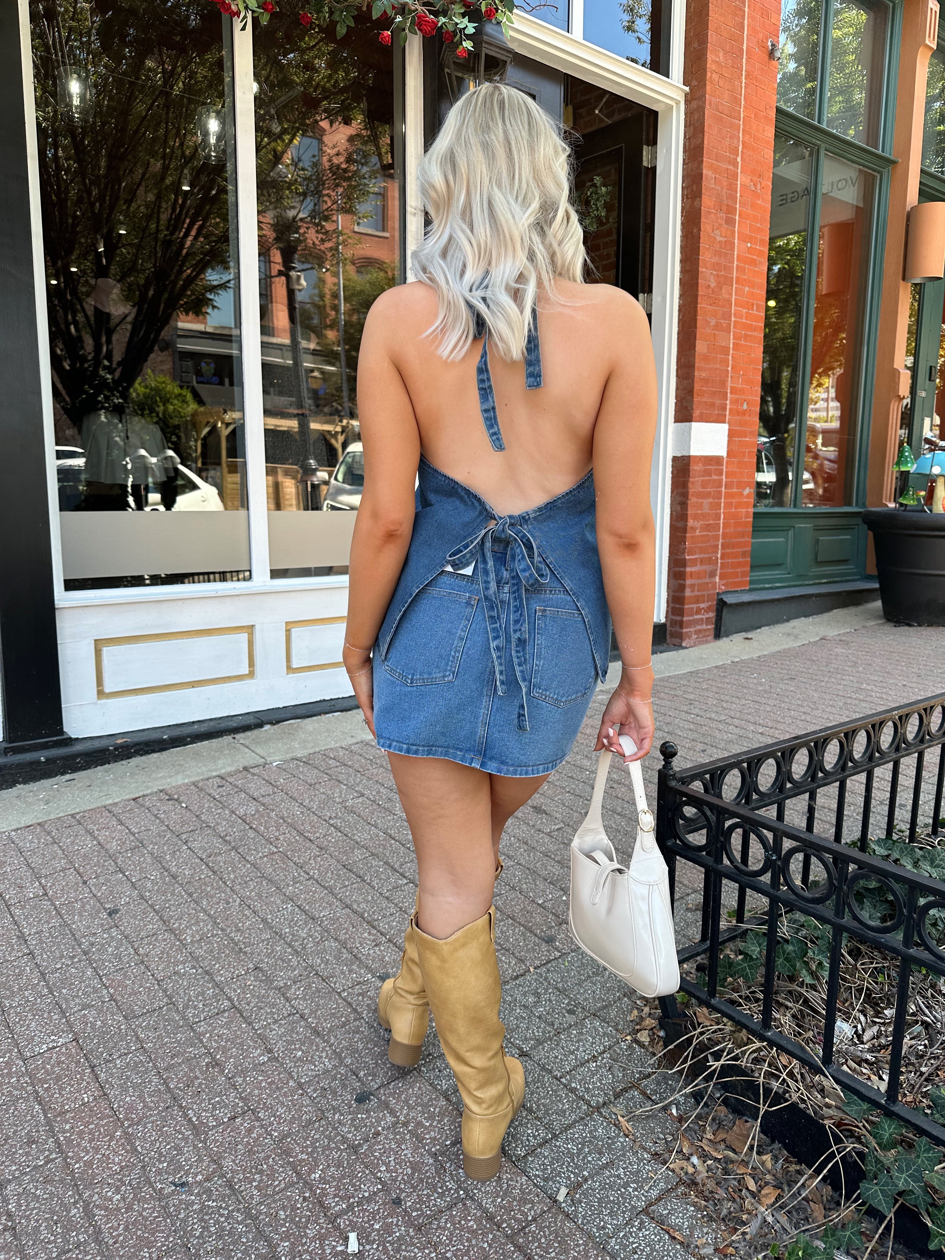 Woman wearing medium wash denim halter top with button closure and open back. 