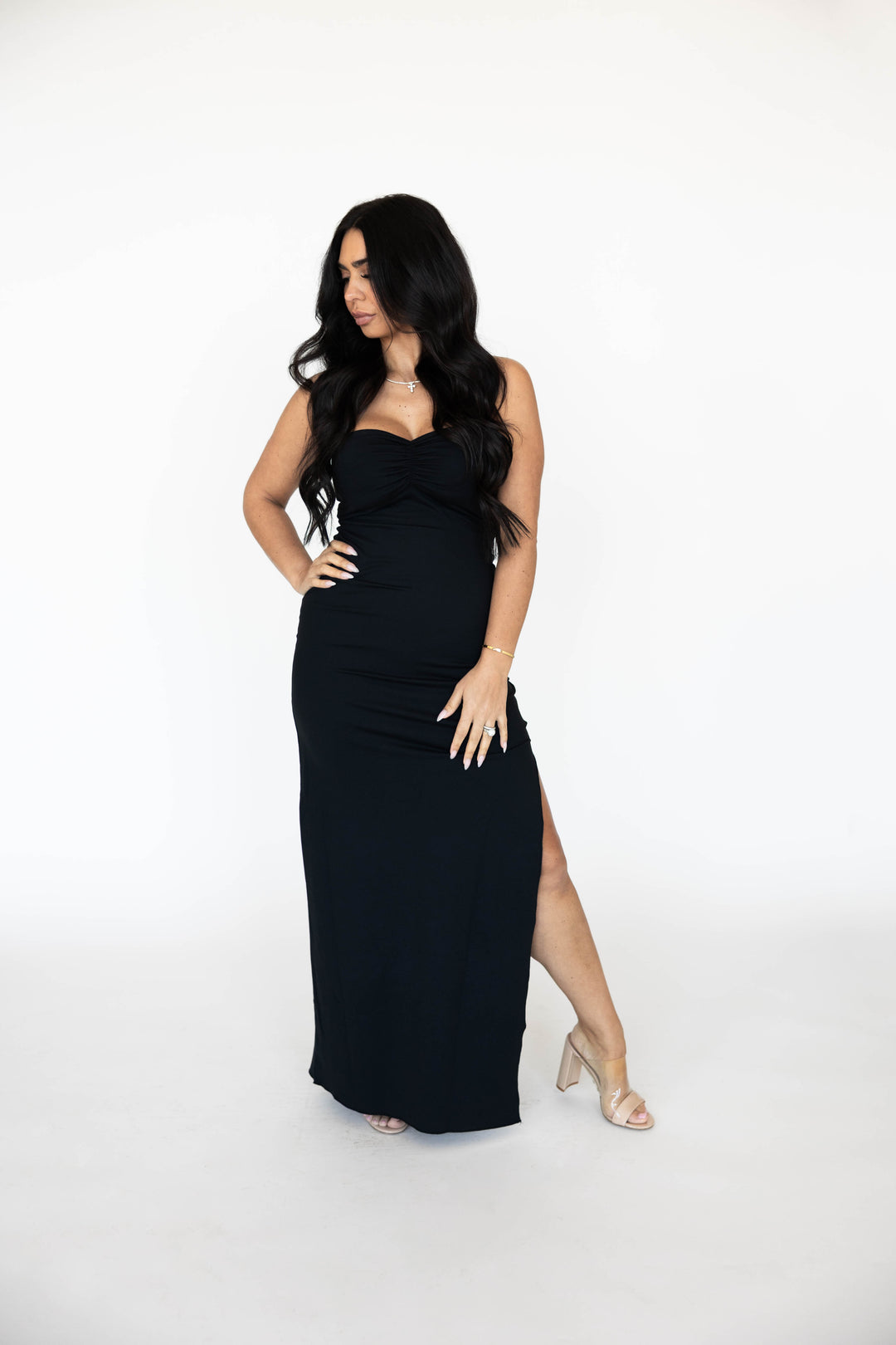 Woman wearing black strapless maxi dress with ruched detailing and side slit.