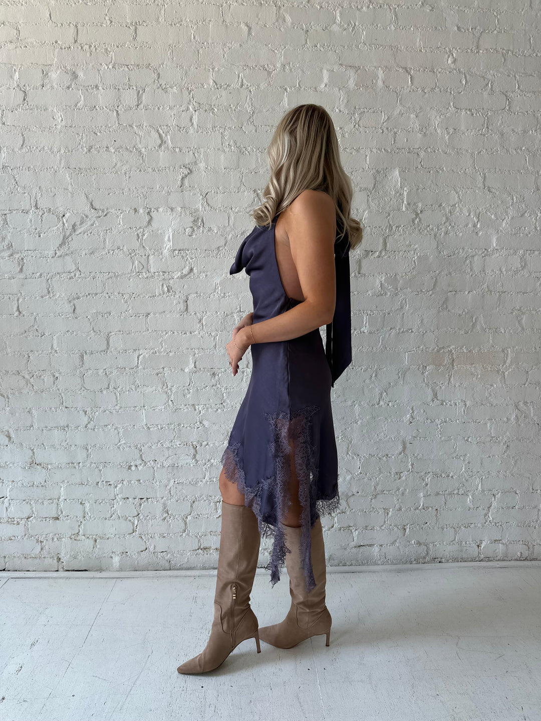 Woman wearing purple satin lace trim midi dress with self tie cowl halter neck. 
