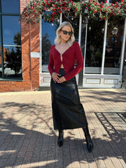 Woman wearing burgundy long sleeve top with twist front and gold detail.