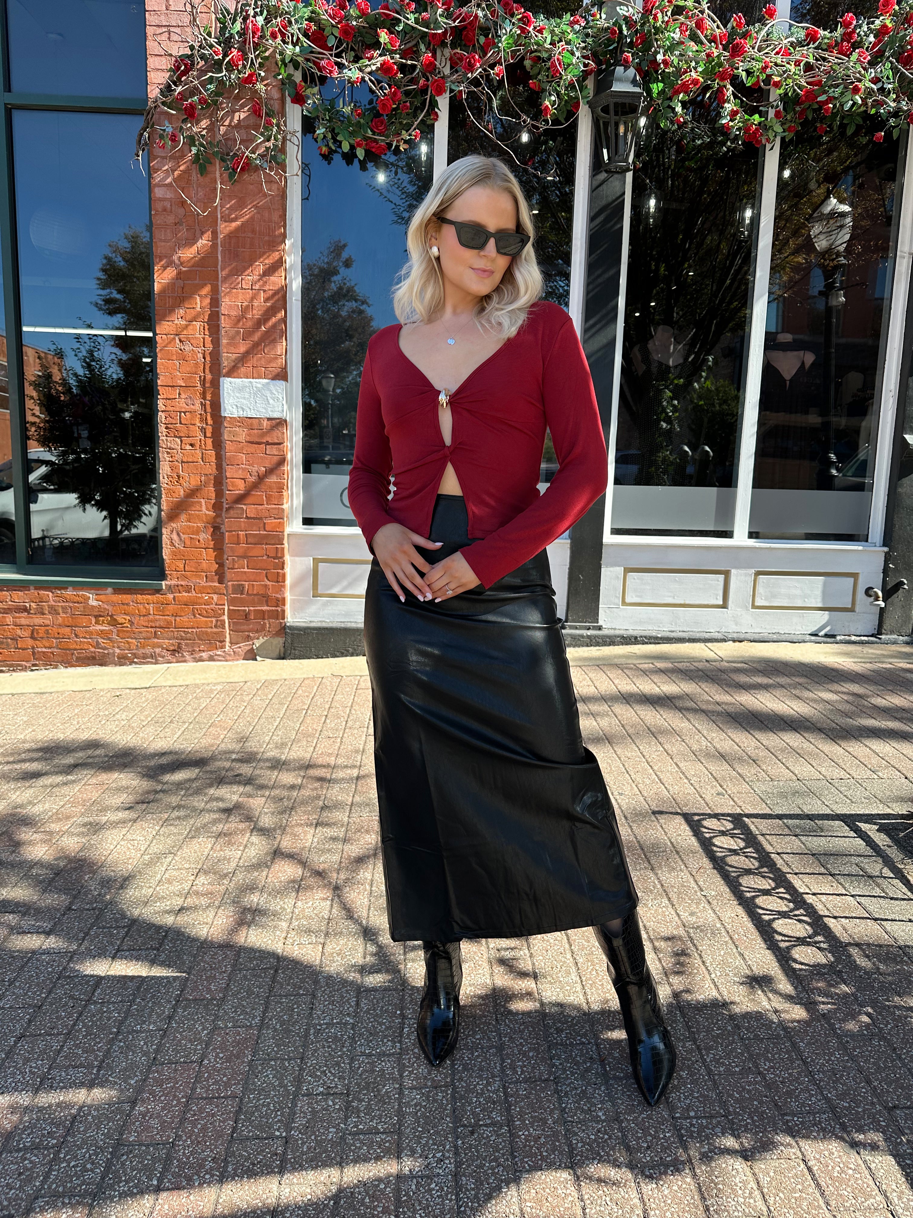 Woman wearing burgundy long sleeve top with twist front and gold detail.