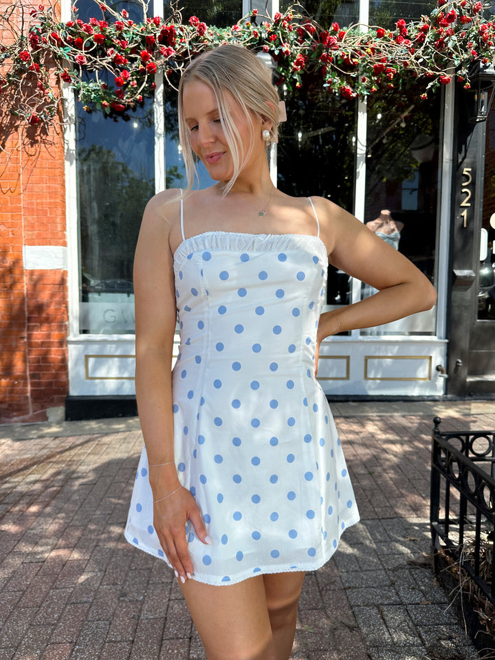 Woman wearing white mini dress with light blue polka dots, and adjustable straps.