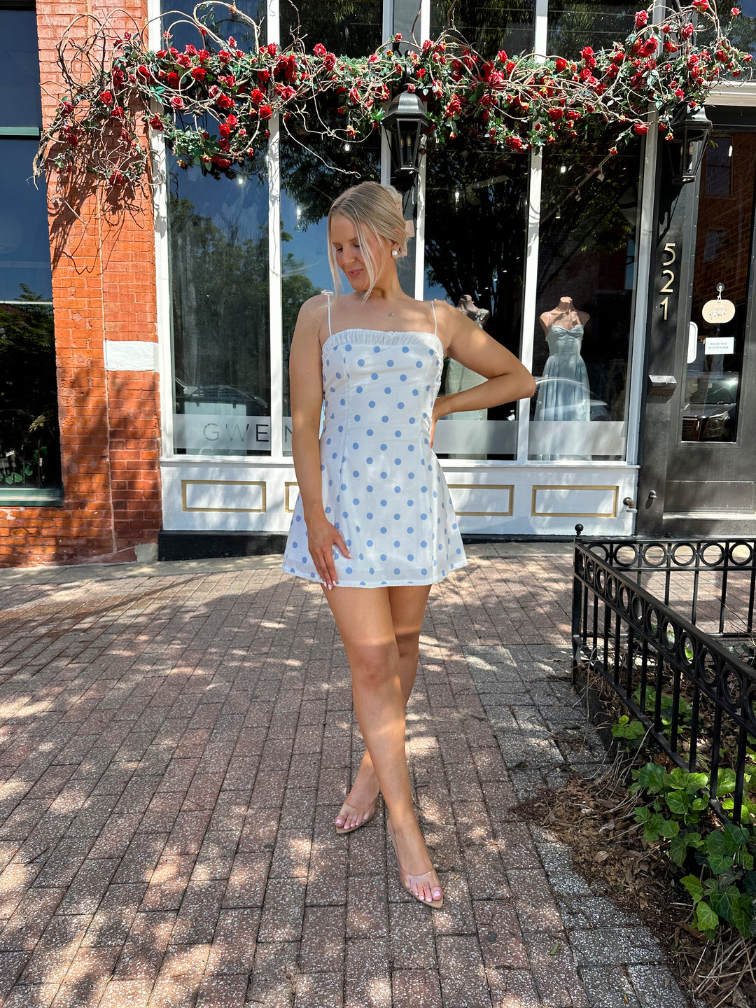 Woman wearing white mini dress with light blue polka dots, and adjustable straps.