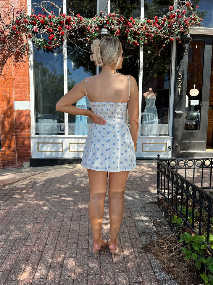 Woman wearing white mini dress with light blue polka dots, and adjustable straps.