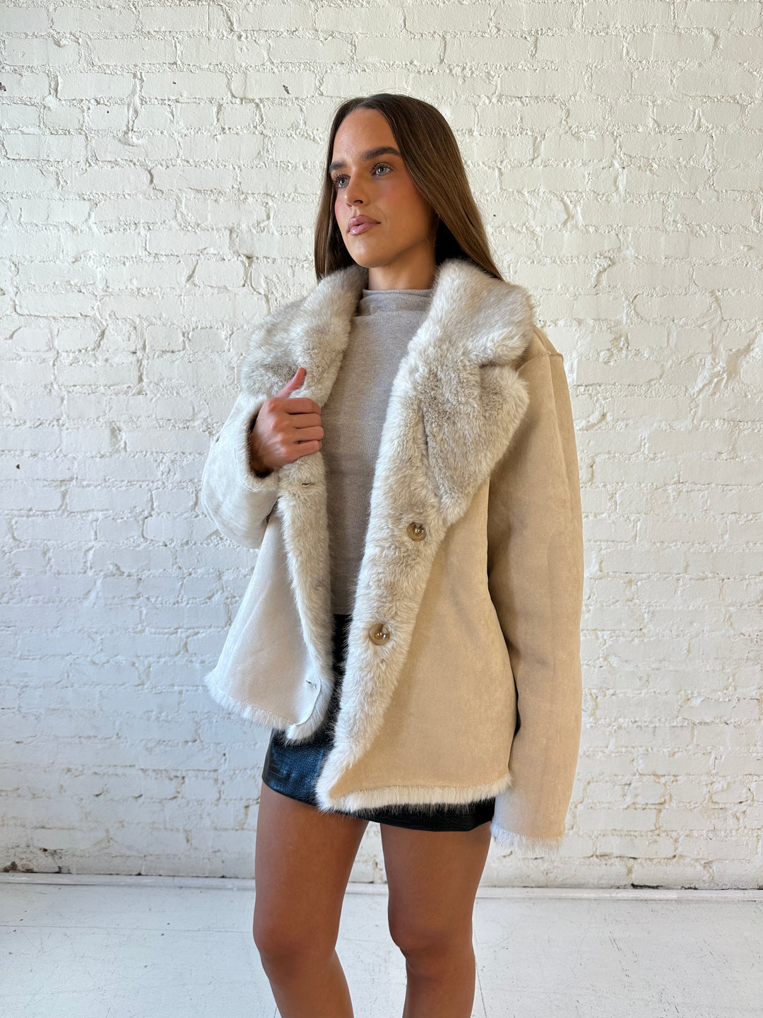 Woman wearing taupe reversible coat with one side being a faux fur, and the other side being suede. 