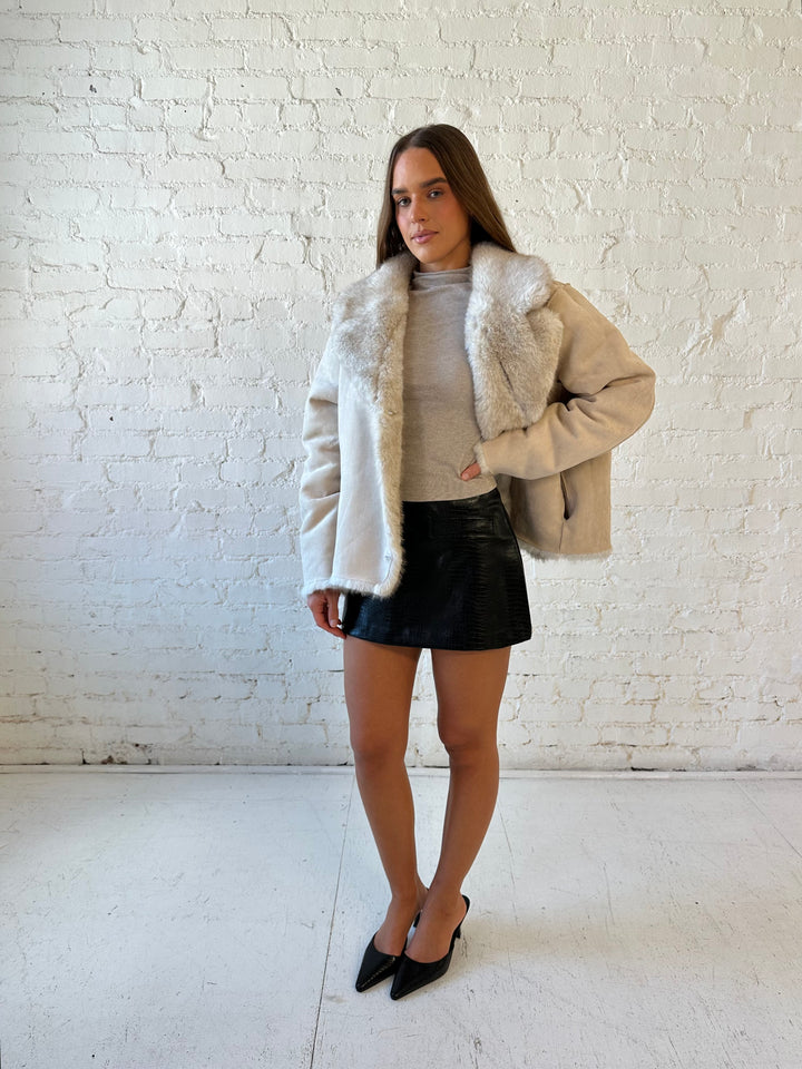 Woman wearing taupe reversible coat with one side being a faux fur, and the other side being suede. 
